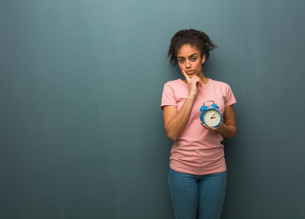 Jovem negra duvidando e confusa. ela está segurando um despertador.