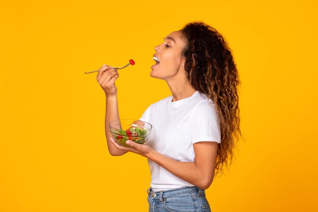 Foto jovem negra em casual desfrutando de uma deliciosa salada vegetariana no estúdio