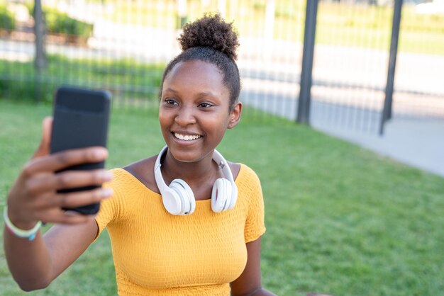 Jovem negra fazendo uma selfie ao ar livre sorrindo brilhantemente para um auto-retrato de mídia social foco nos olhos e no sorriso brilhante