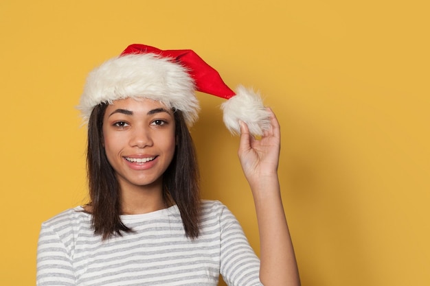 Jovem negra feliz com chapéu de Papai Noel em fundo amarelo