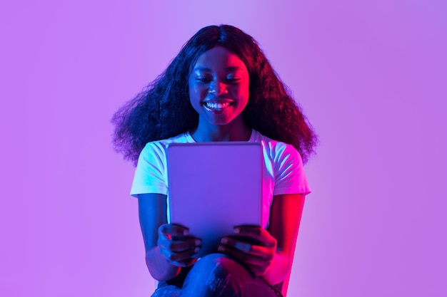 Foto jovem negra focada usando laptop para trabalho on-line ou comunicação em luz neon