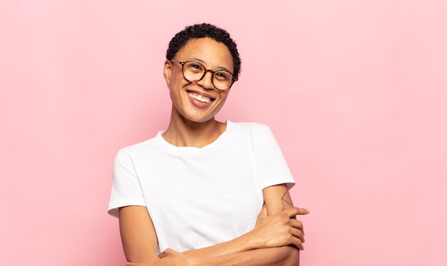 Jovem negra negra rindo alegremente de braços cruzados, numa pose relaxada, positiva e satisfeita