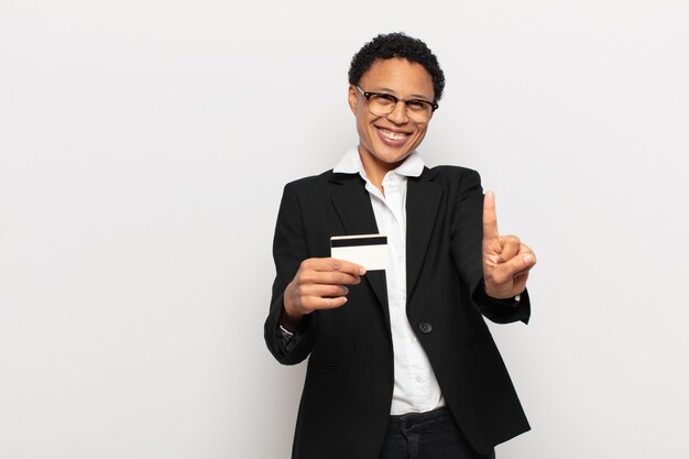 Jovem negra negra sorrindo com orgulho e confiança fazendo a pose número um triunfantemente, sentindo-se uma líder