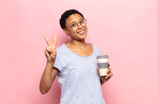 Jovem negra negra sorrindo e parecendo amigável, mostrando o número dois ou o segundo com a mão para a frente, em contagem regressiva