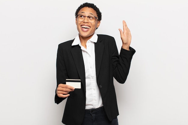 Jovem negra negra sorrindo feliz e alegre, acenando com a mão, dando as boas-vindas e cumprimentando você ou dizendo adeus