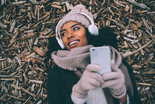 Jovem negra no telefone móvel deitado sobre pedaços de madeira