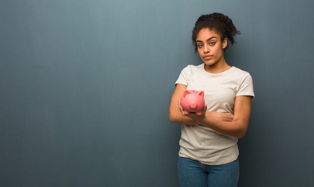 Jovem negra, olhando para a frente. ela está segurando um cofrinho.