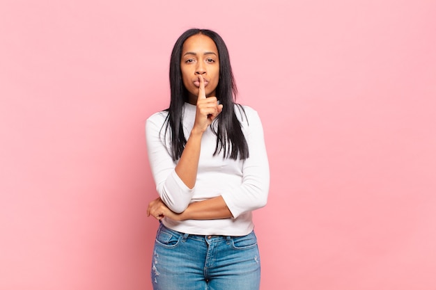 Jovem negra pedindo silêncio e silêncio, gesticulando com o dedo na frente da boca, dizendo shh ou guardando segredo