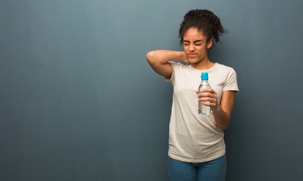Jovem negra que sofre de dor de garganta. ela está segurando uma garrafa de água.