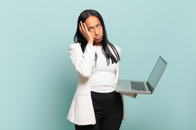 Jovem negra se sentindo entediada, frustrada e com sono depois de uma tarefa cansativa, enfadonha e tediosa, segurando o rosto com a mão. conceito de laptop