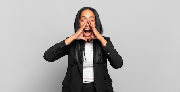 Jovem negra se sentindo feliz, animada e positiva, dando um grande grito com as mãos perto da boca, gritando. conceito de negócios