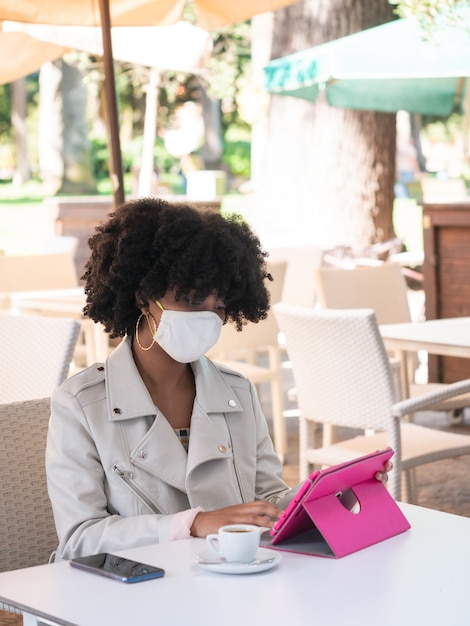 Jovem negra sentada em uma cafeteria enquanto trabalhava com um tablet rosa