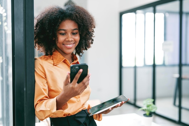 Foto jovem negra sorridente usando telefone celular em pé no escritório