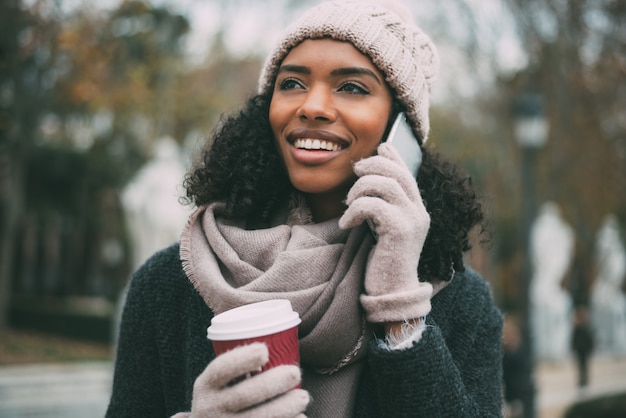 Jovem negra tomando café e falando no telefone celular perto do palácio real no inverno