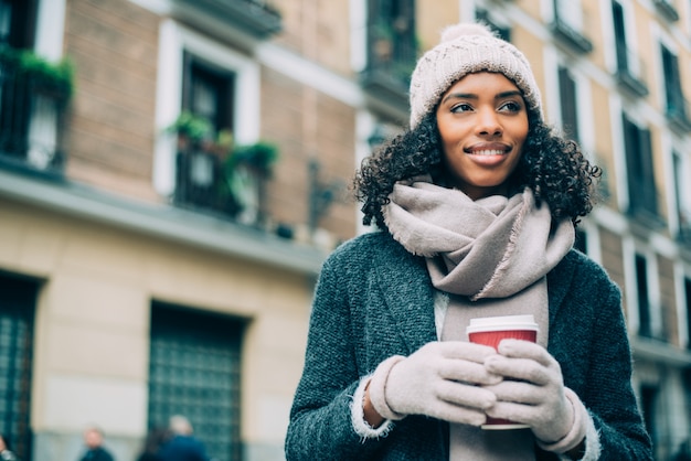 Jovem negra tomando café vagando pelas ruas de madrid no inverno