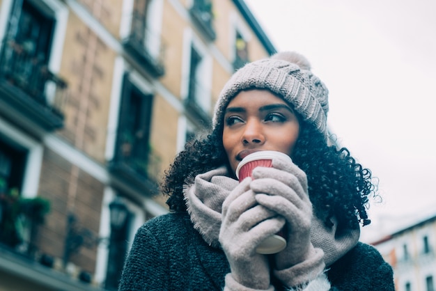 Foto jovem negra tomando café vagando pelas ruas de madrid no inverno