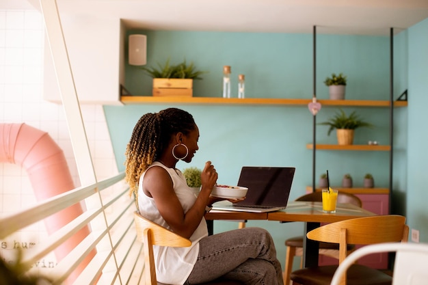 Jovem negra tomando um café da manhã saudável enquanto trabalhava no laptop no café