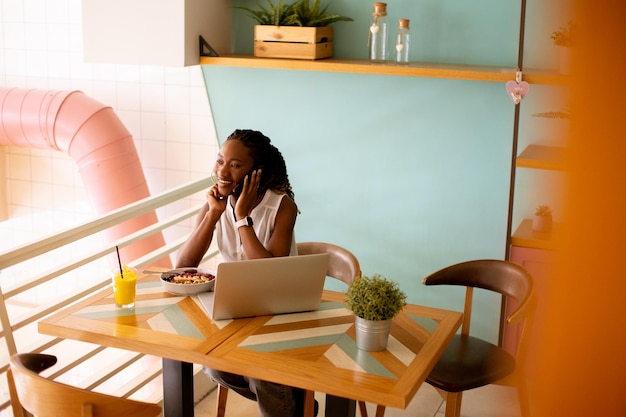 Jovem negra tomando um café da manhã saudável enquanto trabalhava no laptop no café