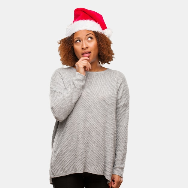 Jovem negra usando um chapéu de Papai Noel duvidando e confuso