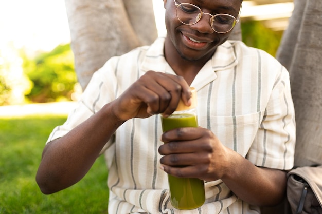 Jovem negro abrindo garrafa de vidro de suco verde ao ar livre