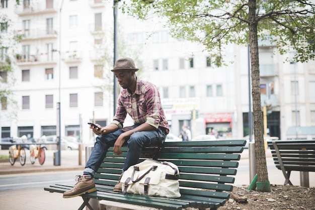 jovem negro afro bonito sentado num banco do lado de fora da cidade