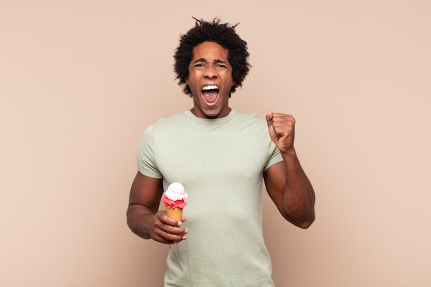 Jovem negro afro gritando agressivamente com uma expressão de raiva ou com os punhos cerrados celebrando o sucesso