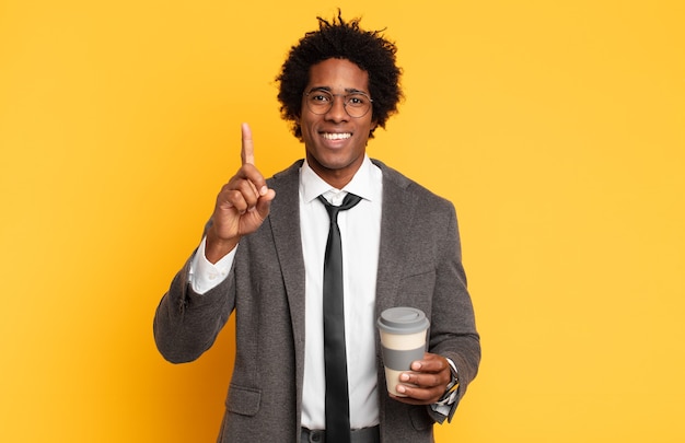 Jovem negro afro sorrindo com orgulho e confiança fazendo a pose número um triunfantemente, sentindo-se um líder