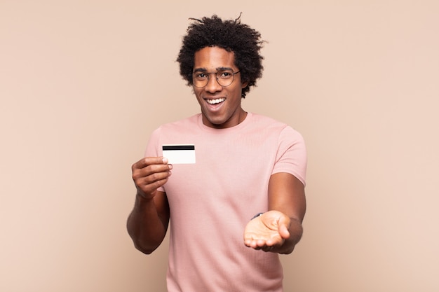 Jovem negro afro sorrindo feliz com um olhar amigável, confiante e positivo, oferecendo e mostrando um objeto ou conceito