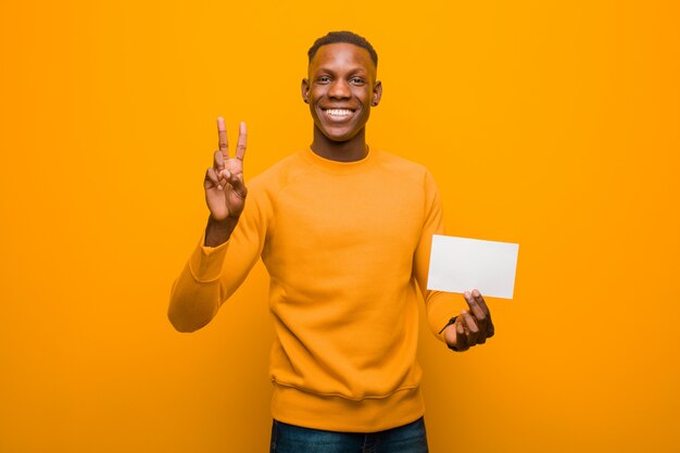 Jovem negro americano africano contra a parede laranja, segurando um cartaz