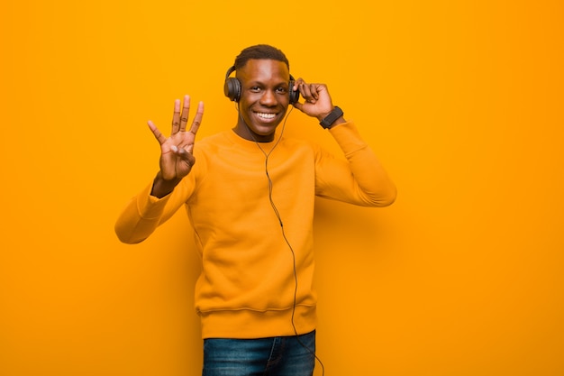 Jovem negro americano africano contra parede laranja com fones de ouvido