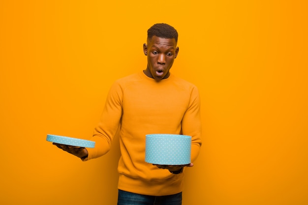 Jovem negro americano africano contra parede laranja com um presente