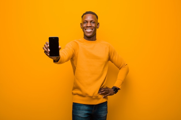 Jovem negro americano africano contra parede laranja com um telefone inteligente