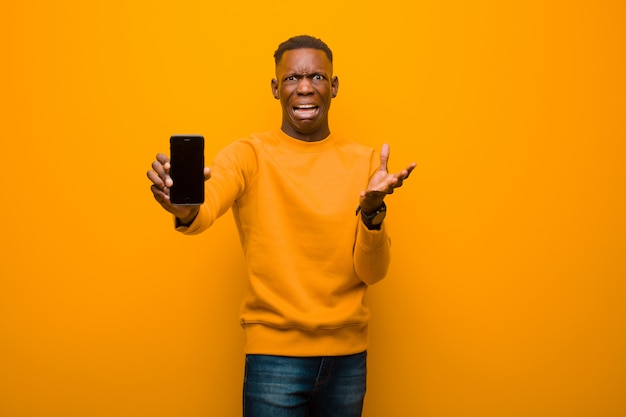 Jovem negro americano africano contra parede laranja com um telefone inteligente