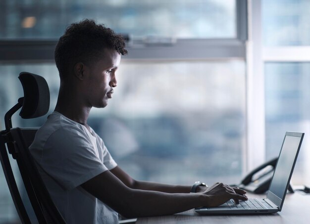 Jovem negro bonito concentrado focado em seu laptop e trabalhando com humor sério em um espaço de cópia de escritório moderno inclui foto de perfil