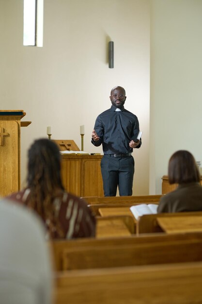 Jovem negro de camisa com colarinho clerical e calças pregando na igreja