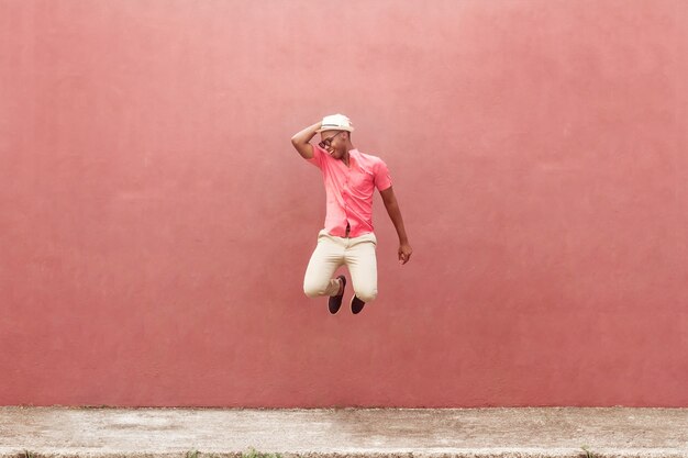 Jovem negro divertido pulando sobre o muro colorido da rua.