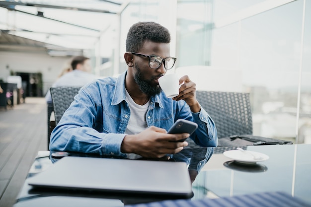 Jovem negro do lado de fora em um café olhando para seu smartphone