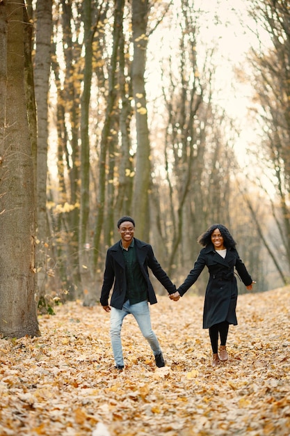 Jovem negro e sua namorada de mãos dadas. casal romântico andando no parque outono. homem e mulher vestindo casacos pretos.