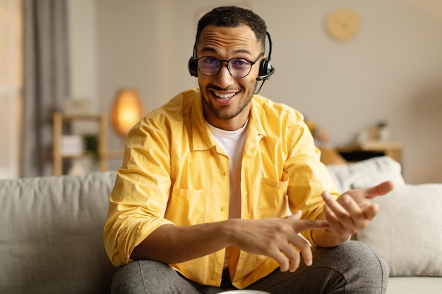 Jovem negro em fones de ouvido tendo videochamada ou conferência de negócios sorrindo para webcam conversando