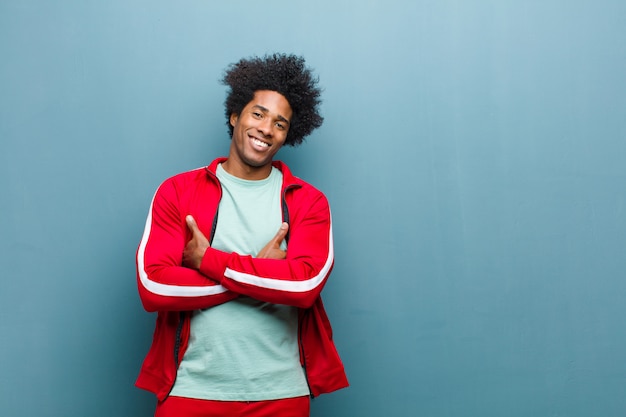 Jovem negro esportes rindo alegremente com os braços cruzados, com uma pose relaxada, positiva e satisfeita contra a parede do grunge