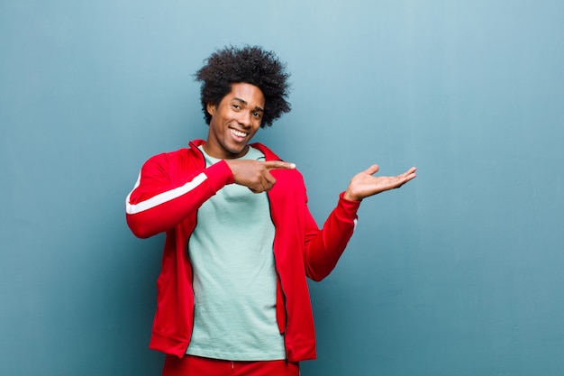 Jovem negro esportes sorrindo alegremente e apontando para copiar o espaço na palma da mão, mostrando ou anunciando um objeto contra a parede do grunge