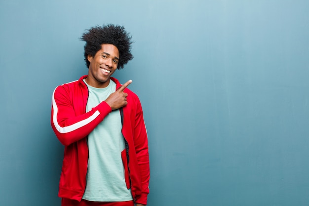 Jovem negro esportes sorrindo alegremente, sentindo-se feliz e apontando para o lado e para cima, mostrando o objeto no espaço da cópia contra a parede do grunge