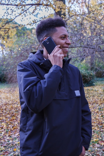 Jovem negro falando ao telefone inteligente na floresta.