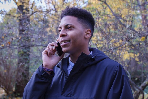 Jovem negro falando ao telefone inteligente na floresta.