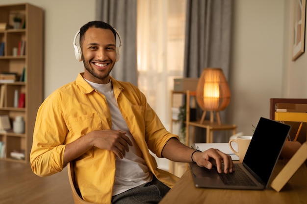 Foto jovem negro feliz em fones de ouvido usando laptop pc com maquete trabalhando on-line em casa copie o espaço