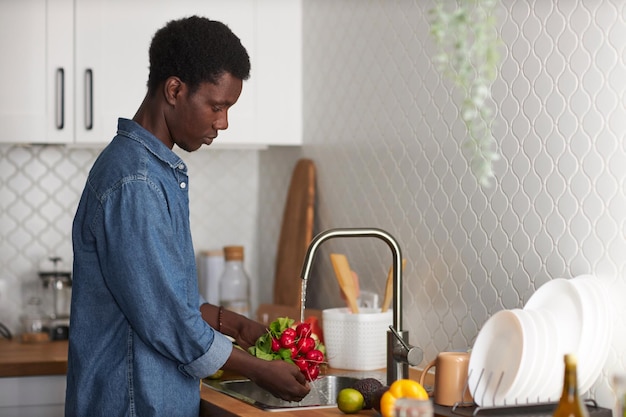 Jovem negro lavando legumes frescos na cozinha