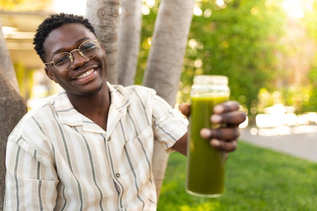 Jovem negro mostrando a garrafa de vidro de suco verde para a câmera foco no rosto do homem