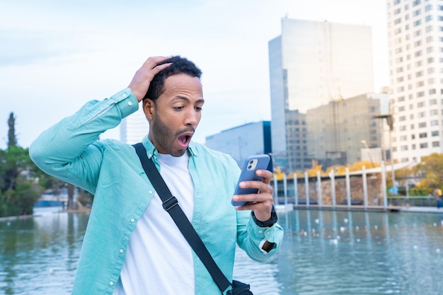 Jovem negro na rua olhando para o telefone com uma expressão de surpresa