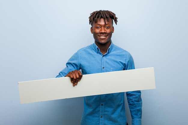 Jovem negro rasta segurando um cartaz feliz, sorridente e alegre.