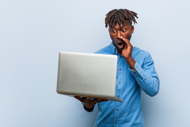 Jovem negro rasta segurando um laptop gritando animado para a frente.